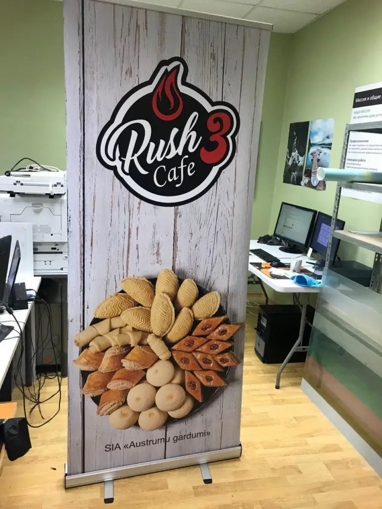 Roll-up stend kohviku logo ja küpsetiste piltidega heledal puidumustriga taustal