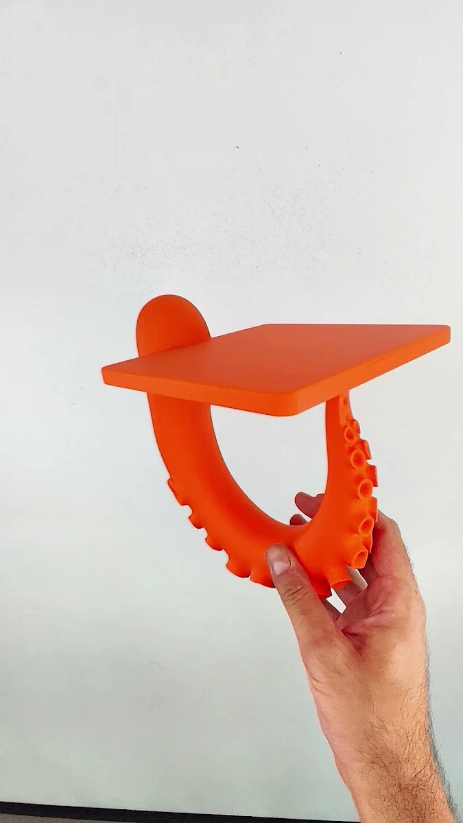 Оранжевая 3D-печатная деталь с изогнутыми элементами в виде щупалец в руке